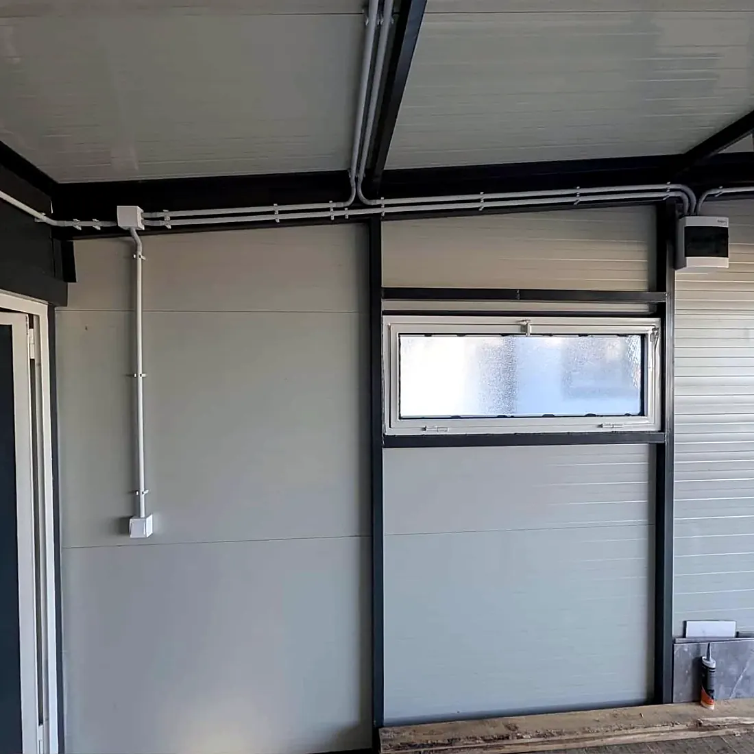 Bijele instalacione cijevi na zidu i konstrukciji sa razvodnom kutijom i malom razdjelnom tablom